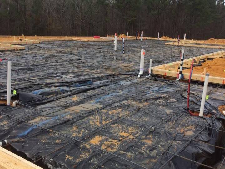 Slab foundation prep with wood forms, black vapor barrier, steel reinforcement and plumbing pipes stubbed up through the slab area