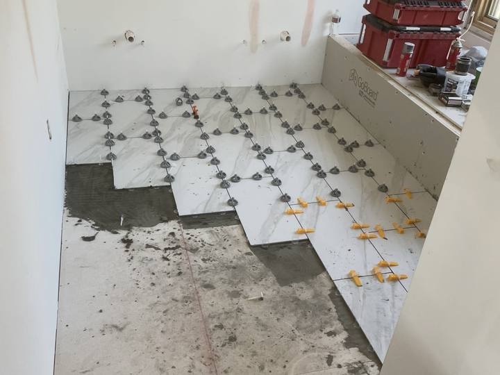 Bathroom remodel in progress with large marble-look floor tiles being laid using leveling clips, next to a tub deck in cement board