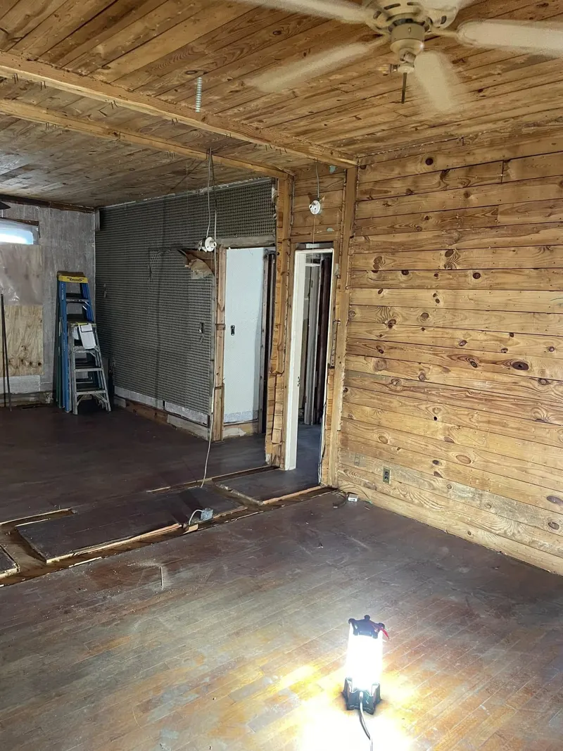 Room with wood plank walls and ceiling, ceiling fan and work light on a bare floor