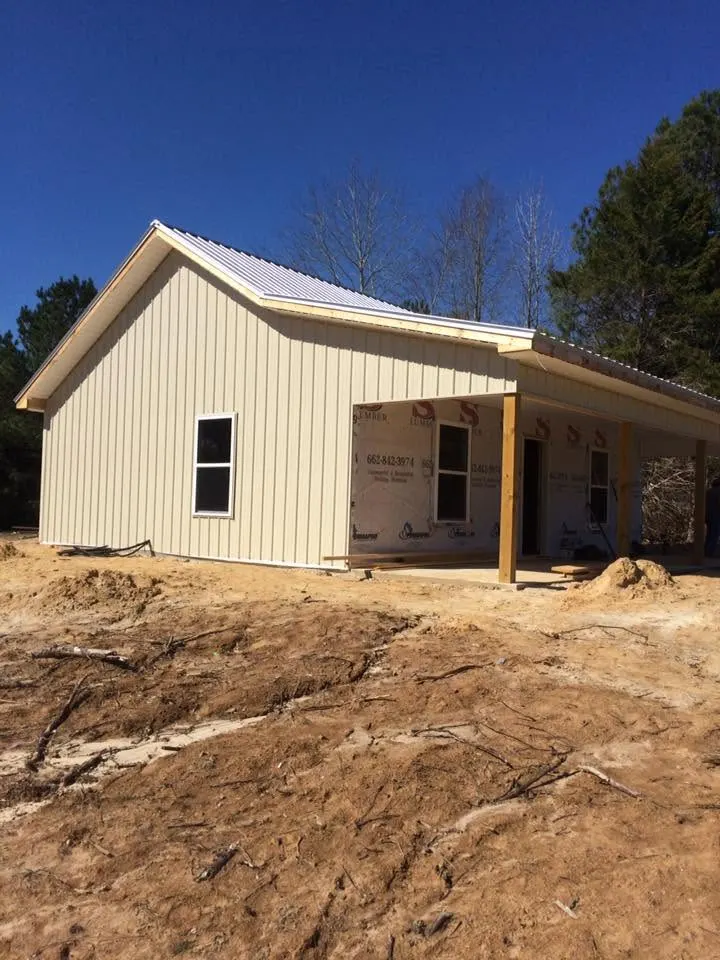 White board-and-batten cottage with metal roof and covered porch on a freshly graded lot
