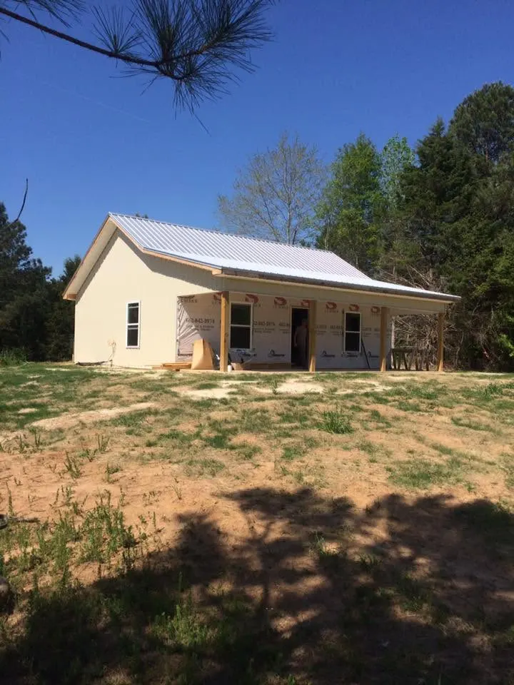 White cottage with metal roof and front porch on a grassy lot