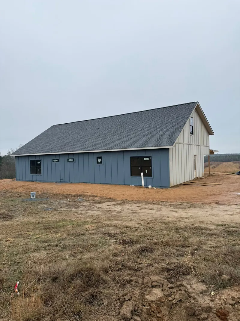 Single-story house with blue siding and dark shingle roof on a freshly graded lot