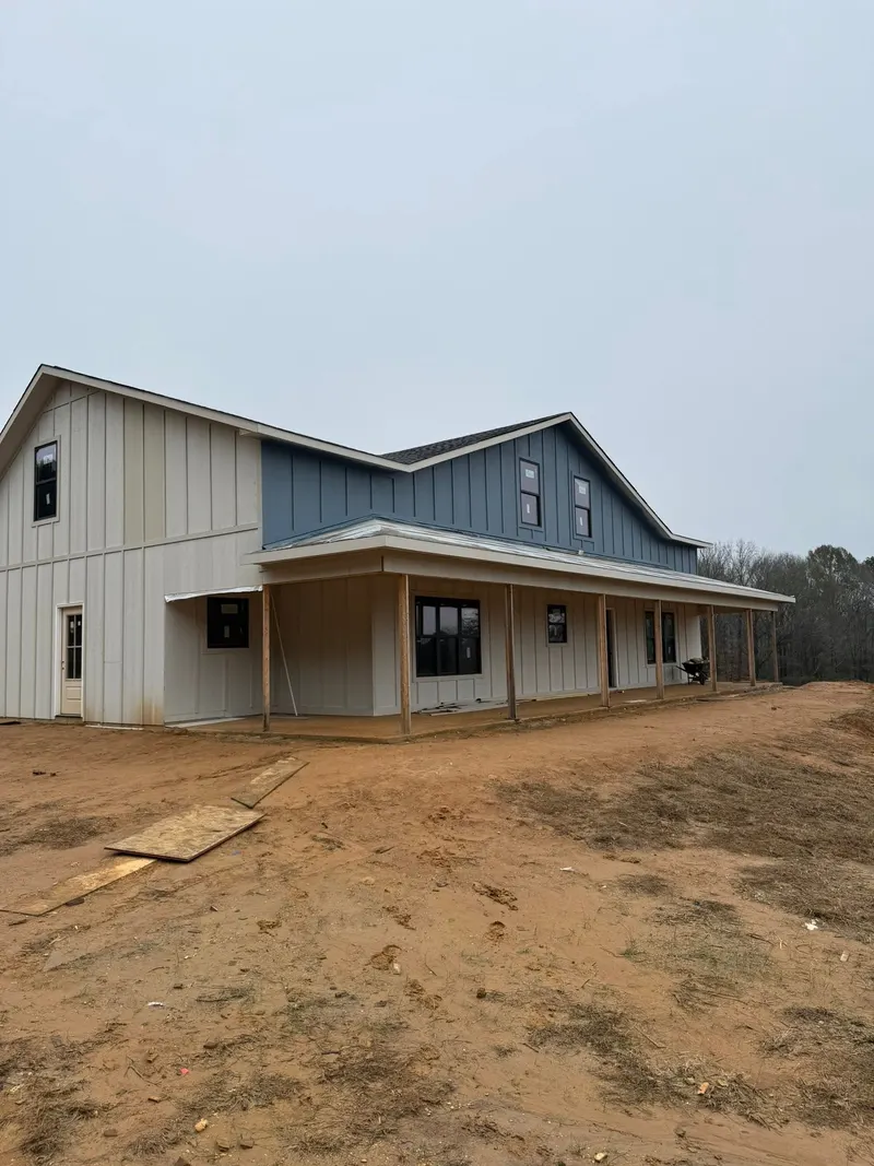 Two-story house with white and blue board-and-batten siding and a wraparound porch on a new lot