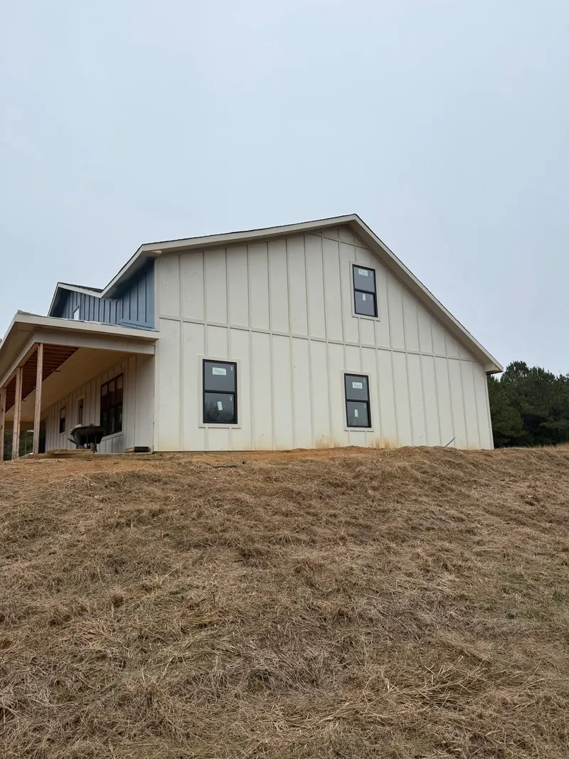 Two-story white board-and-batten house with a covered side porch on a graded lot