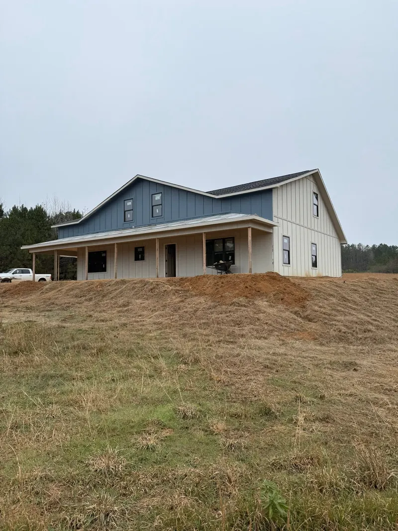 House with blue upper siding, white lower siding and a long front porch on a grassy rise