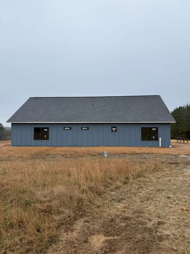 Long single-story house with blue siding and a dark roof under an overcast sky