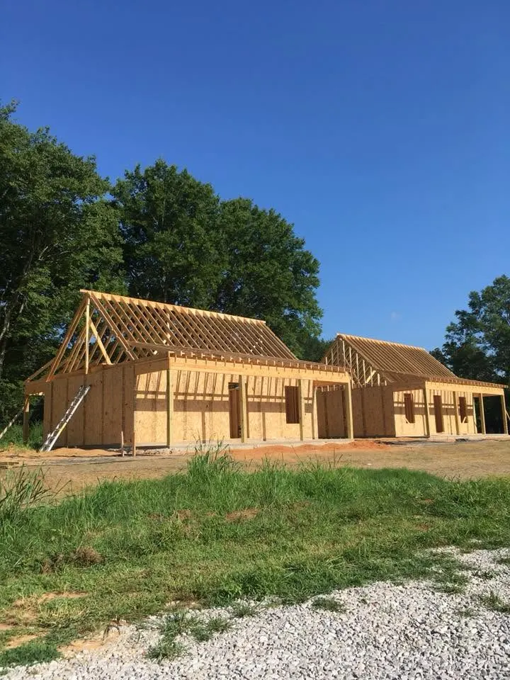 Two wood-framed cottages with roof trusses going up beside a gravel drive