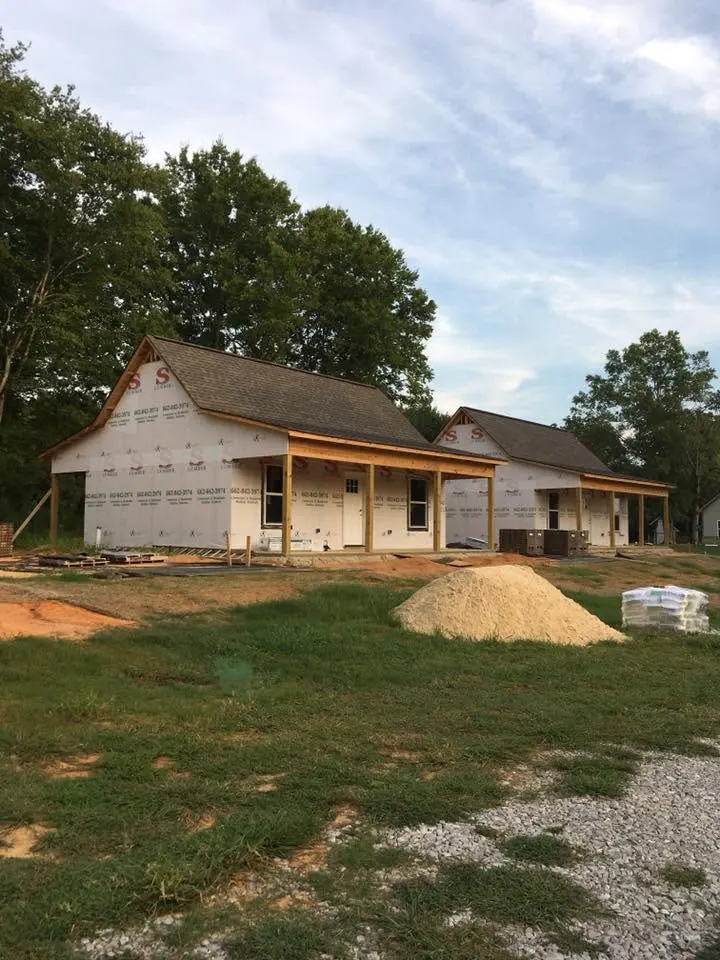 Two cottages closed in with house wrap and roofing, gravel and sand piles in front
