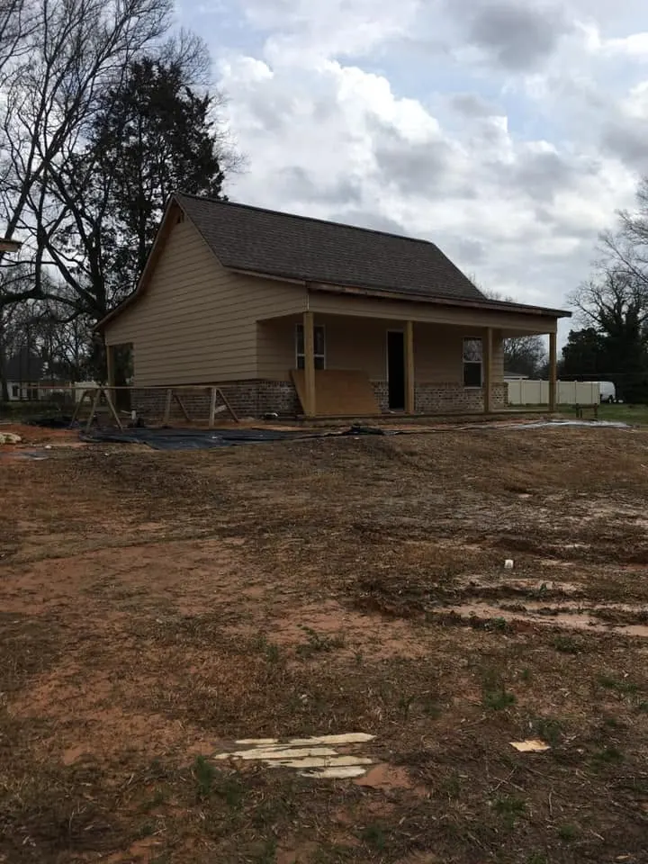 Cottage with new siding, dark roof and front porch on a dirt lot