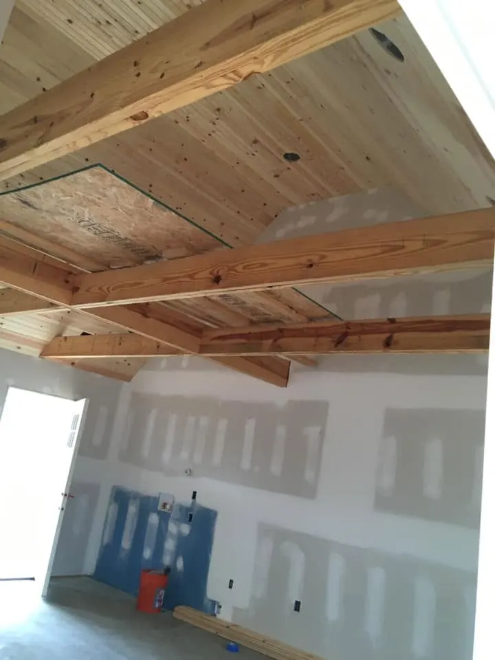 Tongue-and-groove ceiling with wood beams over a room with new drywall