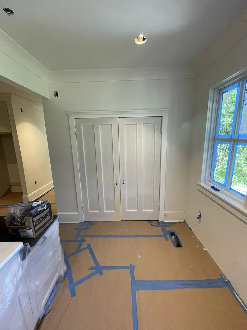 White room with double doors, crown molding and large windows, floors covered for protection