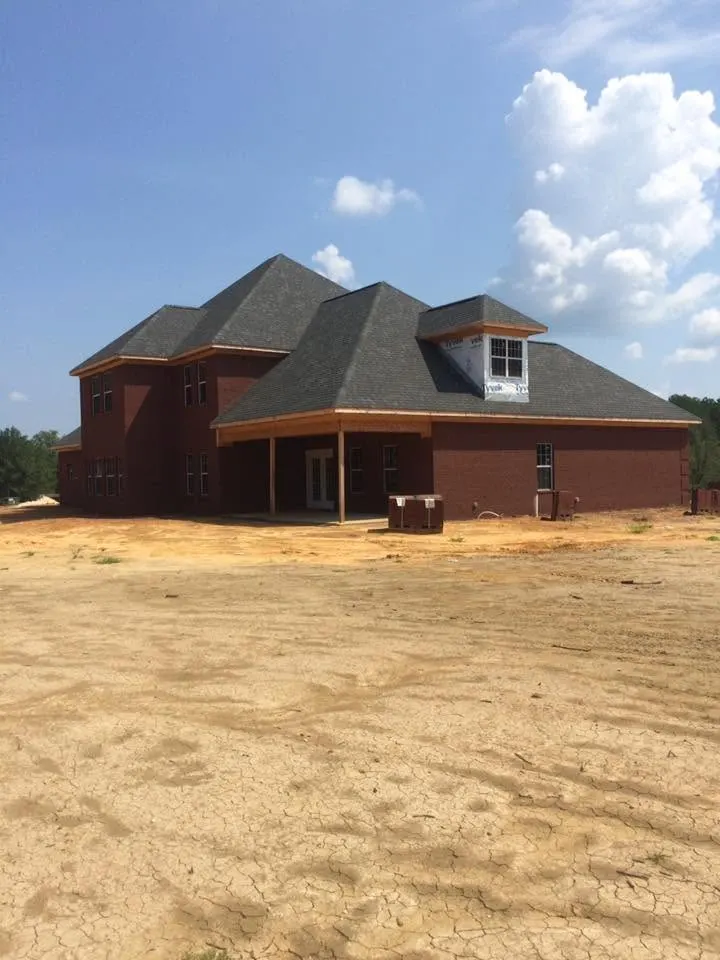 Two-story brick house with dark shingle roof and a covered porch on a bare dirt lot