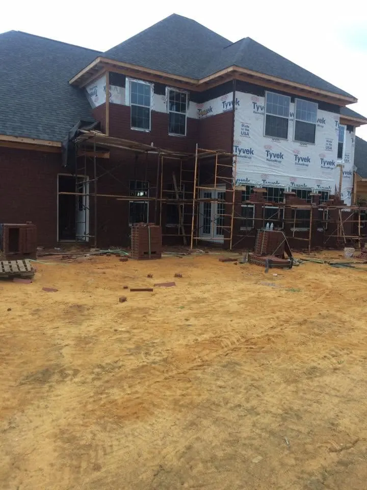 Two-story brick house under construction with scaffolding and house wrap on the upper floor