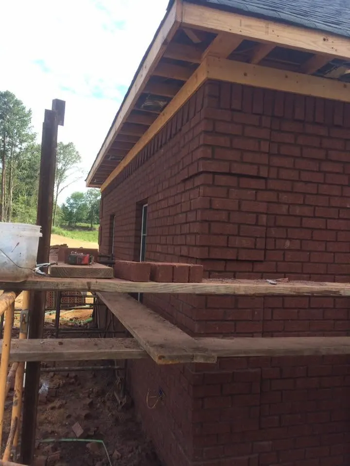 Brick wall and roof framing on a house under construction, with lumber staging along the wall