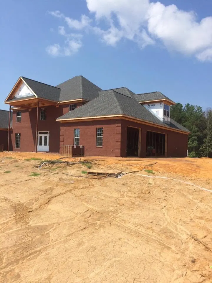 Brick house with gables, a front porch and attached garage on a graded dirt lot