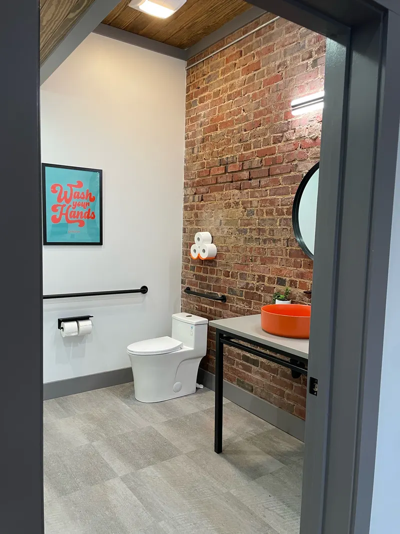 Bathroom with exposed brick wall, wood ceiling, toilet, grab bar and an orange vessel sink