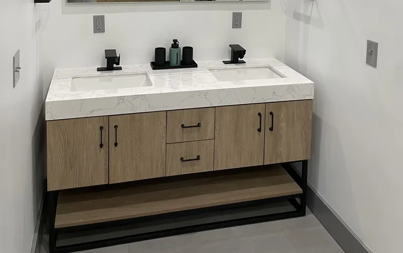 Double vanity with wood-look cabinets, white stone top, two sinks and black faucets on a black metal base
