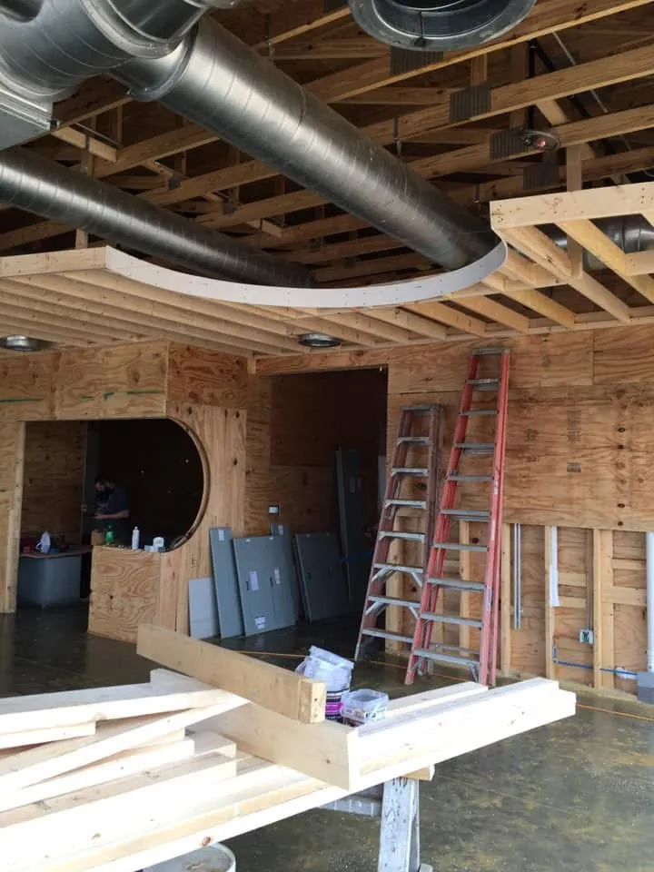Framed interior with plywood walls, a round framed opening, ladders and spiral ductwork overhead