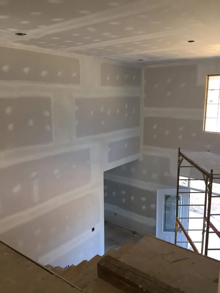 Two-story entry with freshly taped and mudded drywall, seen from the top of the stairs