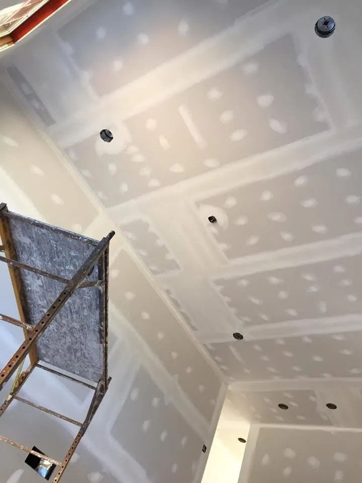 Vaulted ceiling with taped and mudded drywall and recessed light cans, with scaffolding alongside