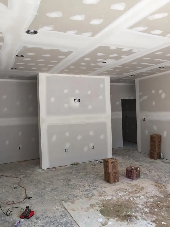 Room with freshly taped and mudded drywall on the walls and ceiling, boxes and tools on the floor