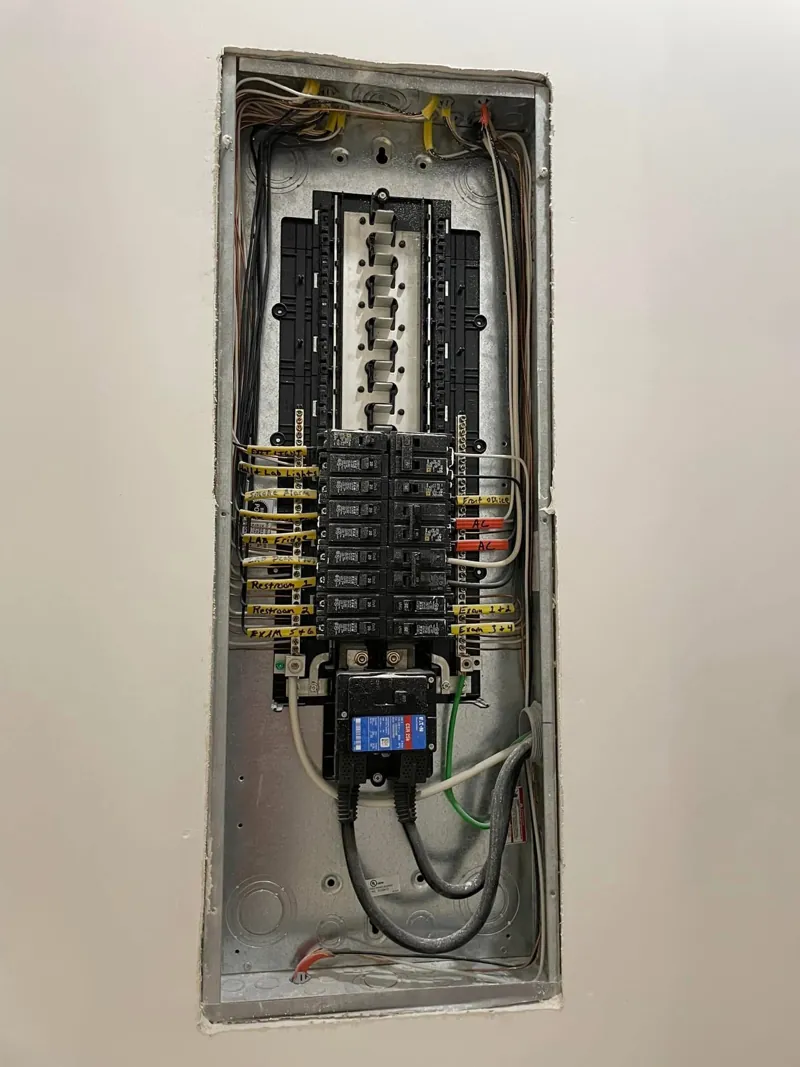 Finished electrical panel with neatly labeled breaker circuits and dressed wiring, set in a new drywall wall