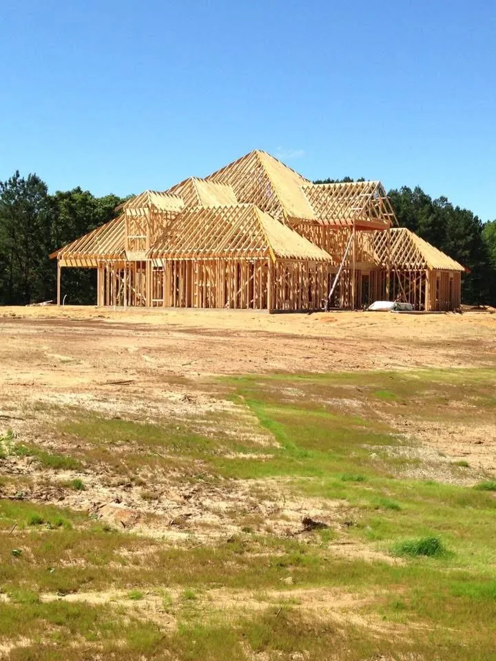 Wood-framed house with multiple roof gables in front of a tree line under a blue sky