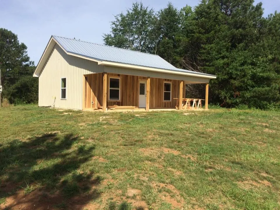 Small finished house with light metal siding, a metal roof and a wood front porch on a grassy lot