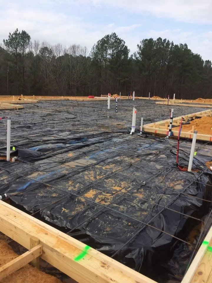 Slab foundation forms with black vapor barrier, rebar grid and plumbing pipes stubbed up before the pour