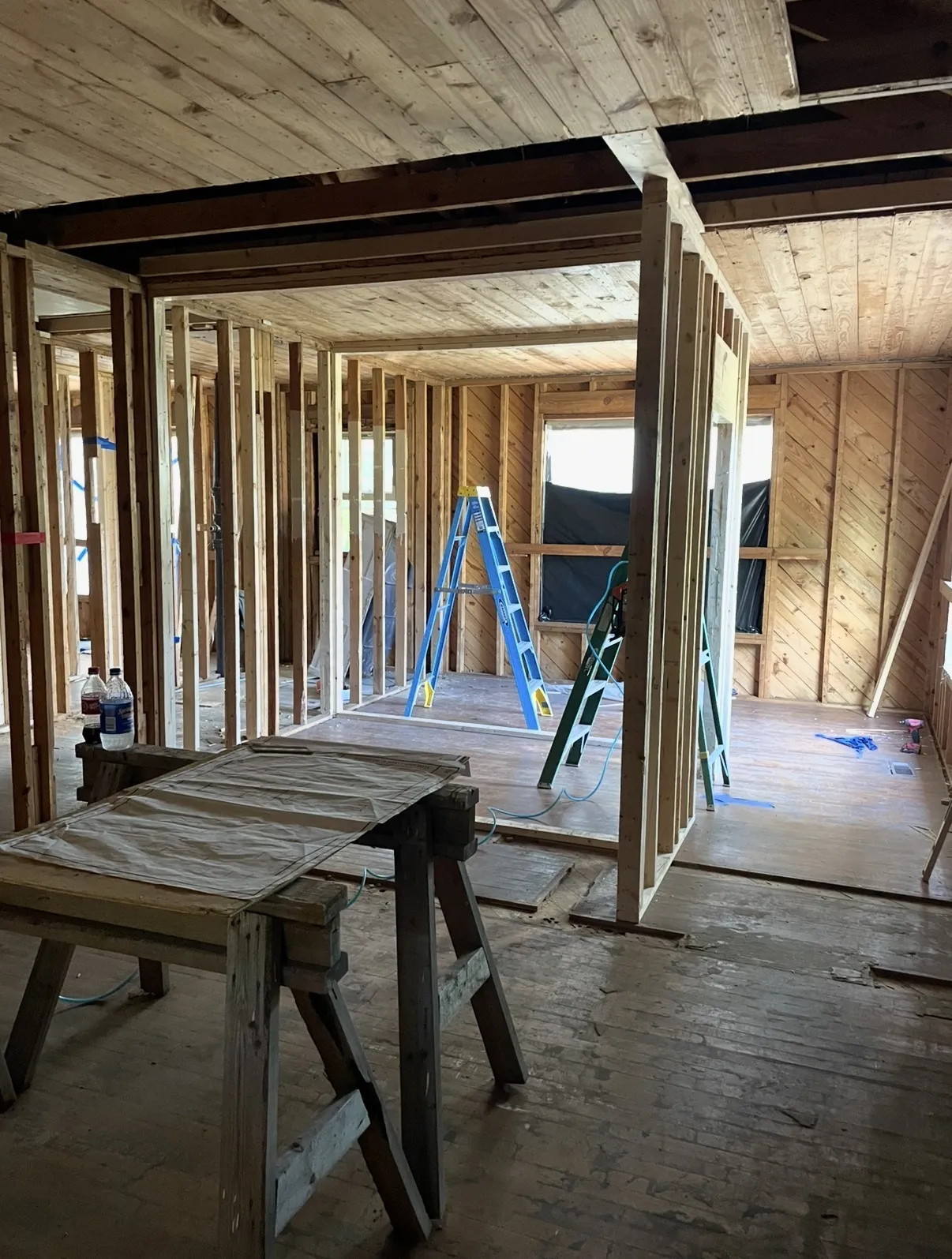 Interior remodel framing with a new stud wall, tongue-and-groove wood ceiling, workbench and stepladders in adjoining rooms