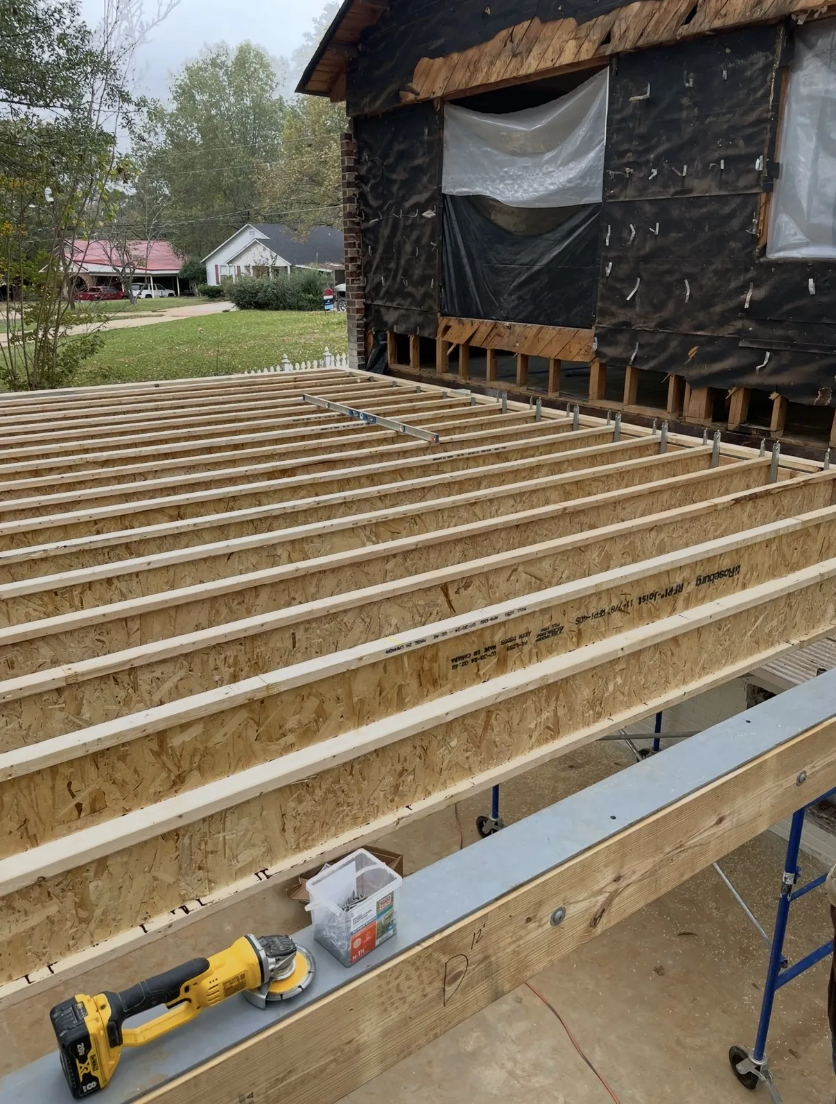 Wood I-joists for a deck or porch addition attached to the house with metal hangers, a spirit level across two joists